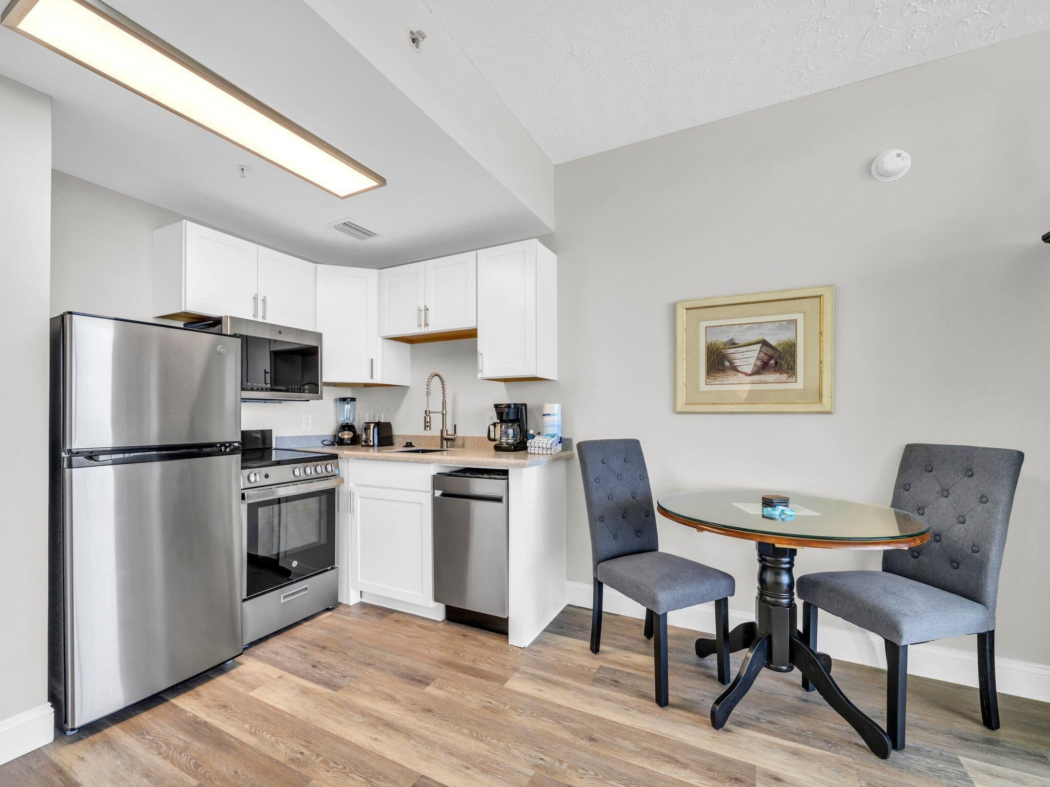 A modern kitchen with stainless steel appliances, white cabinetry, and a wooden floor.