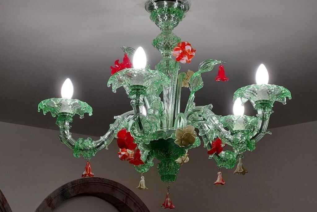 Een kroonluchter met meerdere armen en kaarsachtige lampen, versierd met rode en groene bloemmotieven.