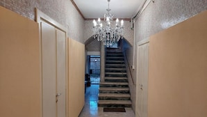 Um corredor com lustre, escada e portas em ambos os lados.