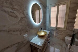 A bathroom with a marble vanity, a round mirror with lighting, a toilet, and a window with frosted glass. - Donini Residence in Venice, Suite 1 (venezia)