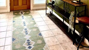 A hallway with a wooden door, a glass ceiling, a green wall, a console table, and a patterned rug. - Rest In Peace on Perkins (San Marcos)