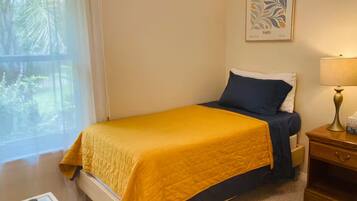 Un dormitorio con cama, una mesita de noche con lámpara, un cuadro en la pared y una ventana con vistas a zonas verdes.