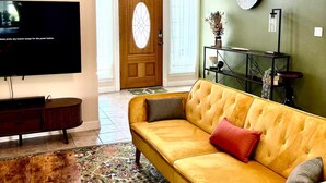 A living room with a yellow sofa, a wooden coffee table, a TV, and a patterned rug. - Rest In Peace on Perkins (San Marcos)
