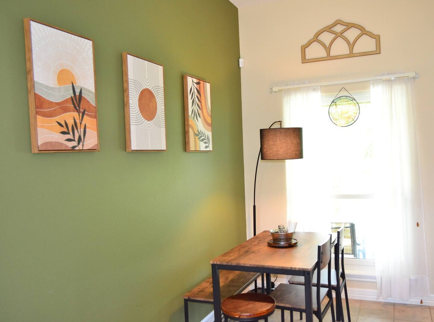 A dining area with a wooden table and chairs, a lamp, and three artworks on the wall.