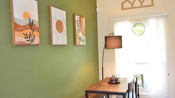 A dining area with a wooden table and chairs, a lamp, and three artworks on the wall.