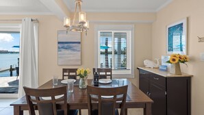 A dining area with a table set for four, a chandelier, and a view of the ocean through a window. - Coastal Breeze Siesta - Manatee (Siesta Key)