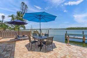 A patio with a table and chairs, a blue umbrella, and a view of a lake. - Coastal Breeze Siesta - Manatee (Siesta Key)