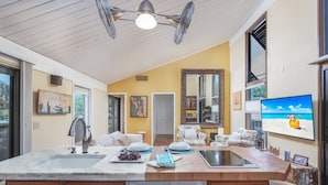 A kitchen with a large island, wooden cabinets, a sink, and a dining area with chairs. - Little Sandy Cove Paradise (Siesta Key)