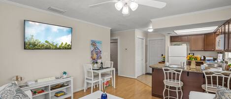 A modern living room with a dining area, kitchen, and a ceiling fan.