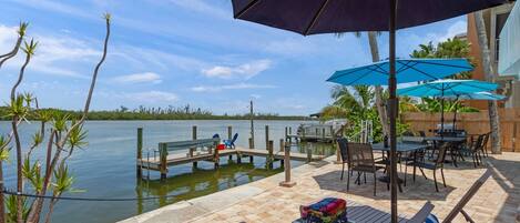 A waterfront patio with lounge chairs, umbrellas, and a dock extending into a lake.