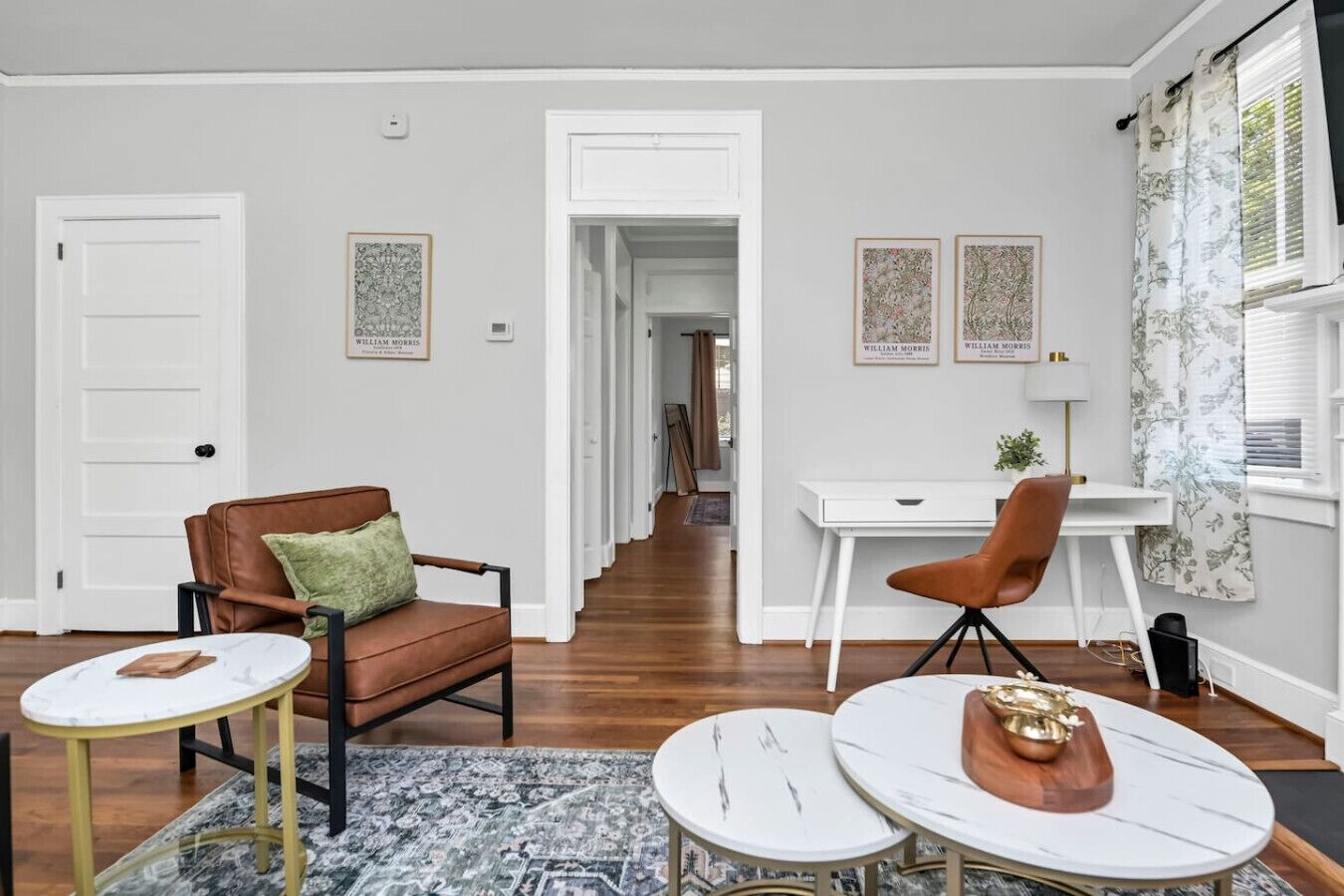 Un salon spacieux avec un canapé en cuir marron, un bureau blanc et une table à manger agrémentée d’un vase décoratif.