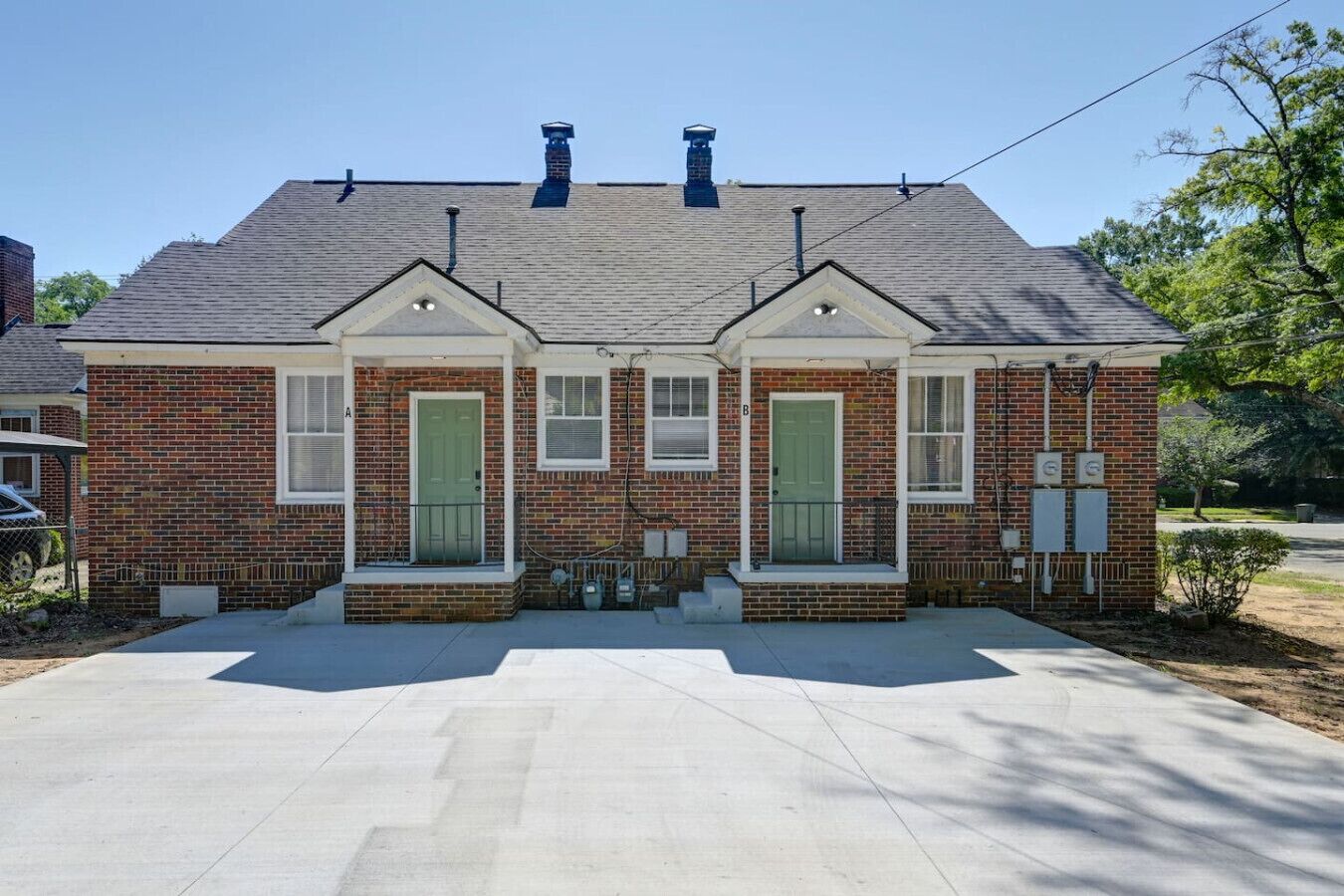 A two-story brick house with a front porch, two green doors, and a chimney.