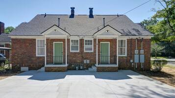 A two-story brick house with a front porch, two green doors, and a chimney.