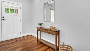 A hallway with a white door, a wooden console table with a mirror, a small plant, and a wicker basket.