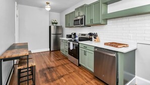 A compact kitchen with green cabinets, a stainless steel refrigerator, a microwave, and a dishwasher.
