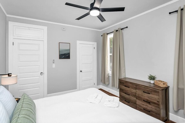 Une chambre à coucher avec un lit, un ventilateur de plafond, une commode et une fenêtre avec des rideaux.