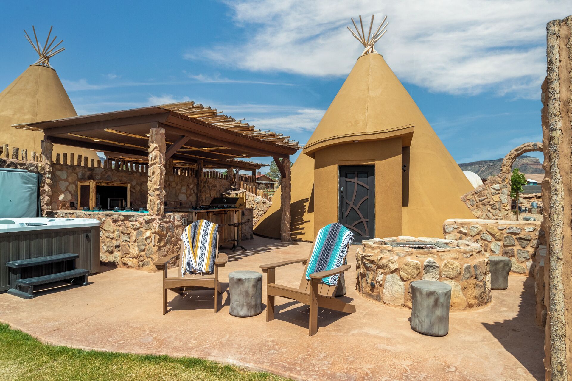 Un chalet doté de deux structures coniques, d’un espace extérieur couvert avec des sièges et d’un mur en pierre.