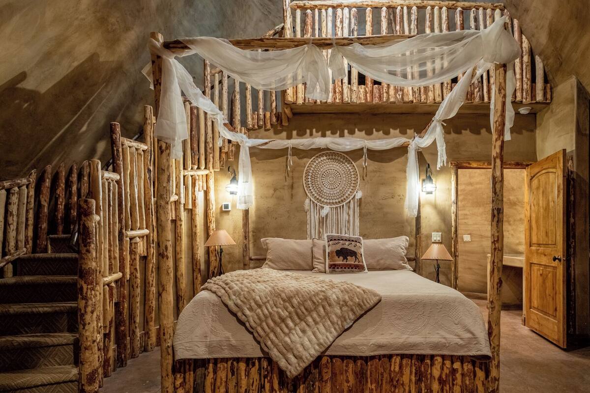 A rustic bedroom with a canopy bed, wooden walls, and a dreamcatcher decoration.