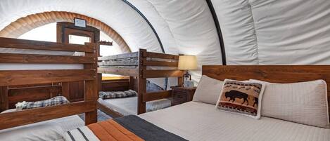 A tented accommodation with bunk beds, a bedside table with a lamp, and a bed with a buffalo-themed pillow.