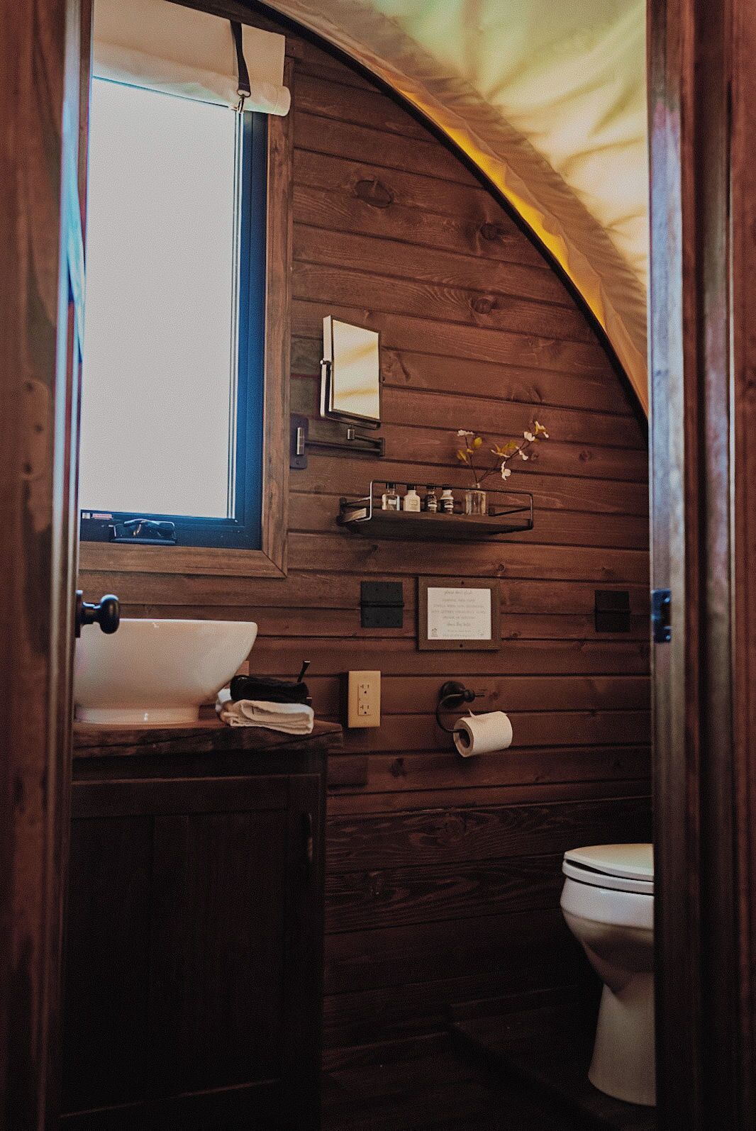A compact wooden bathroom with a sink, mirror, and toilet.