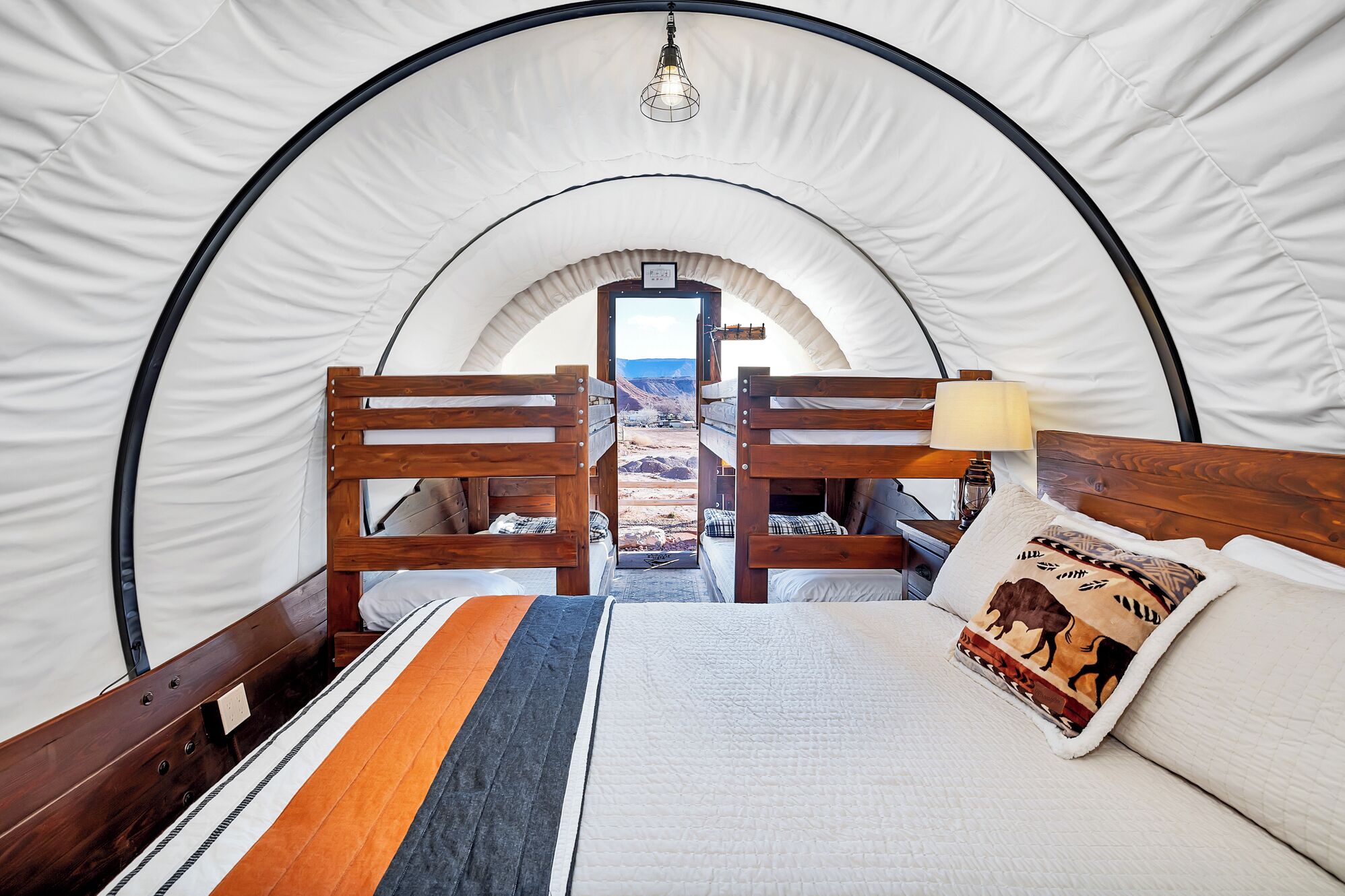 A tented room with a bed, wooden headboard, and a view of a mountainous landscape.