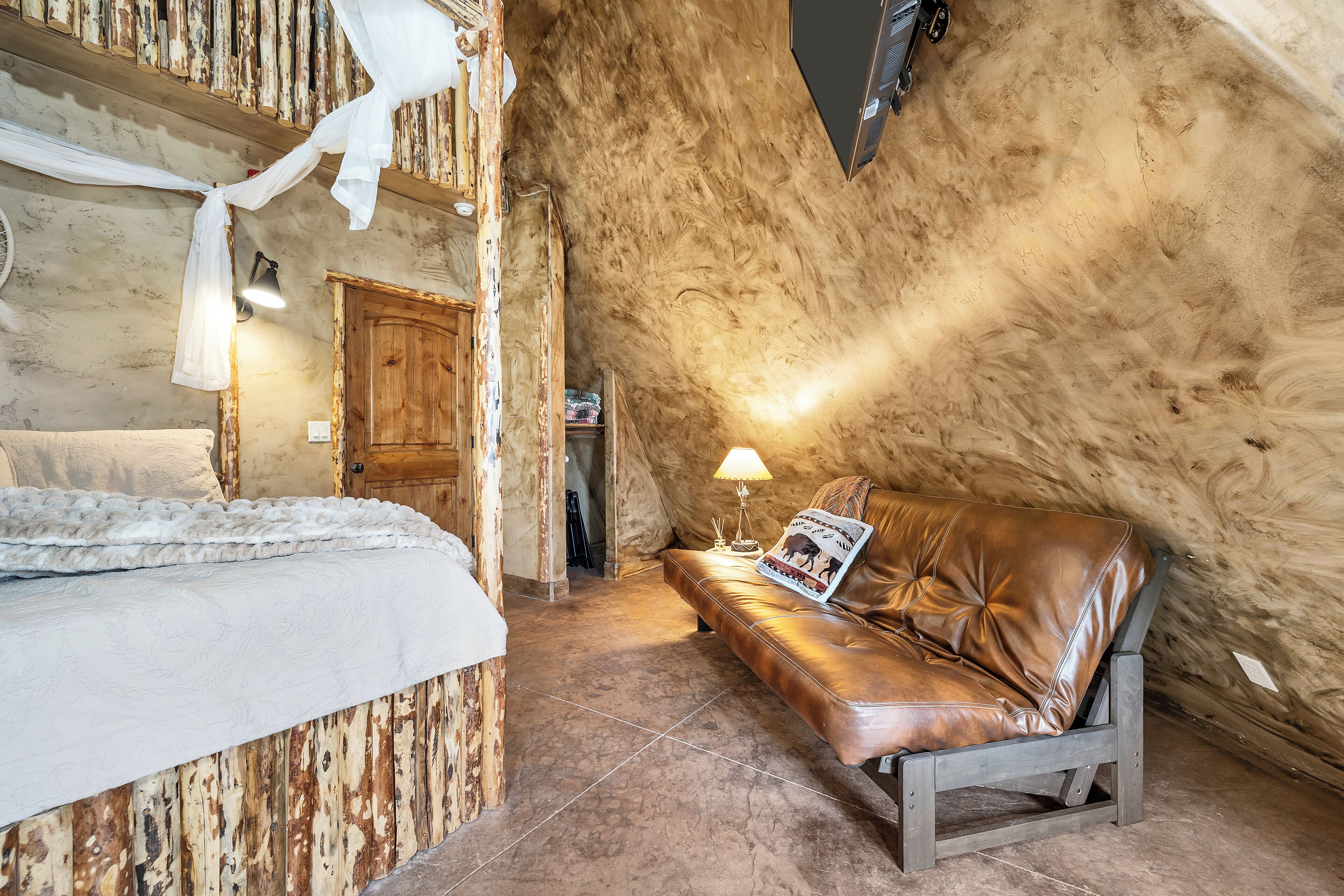 A rustic room with a bed, a leather sofa, and a wooden door.
