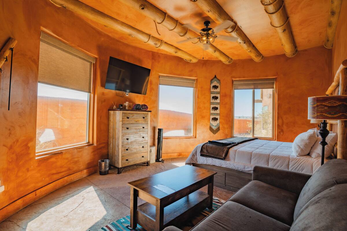 A cozy room with a bed, a sofa, a TV, and a wooden ceiling.