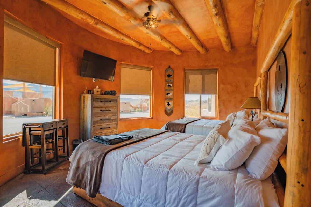 A log cabin bedroom with two beds, a desk, and a TV.