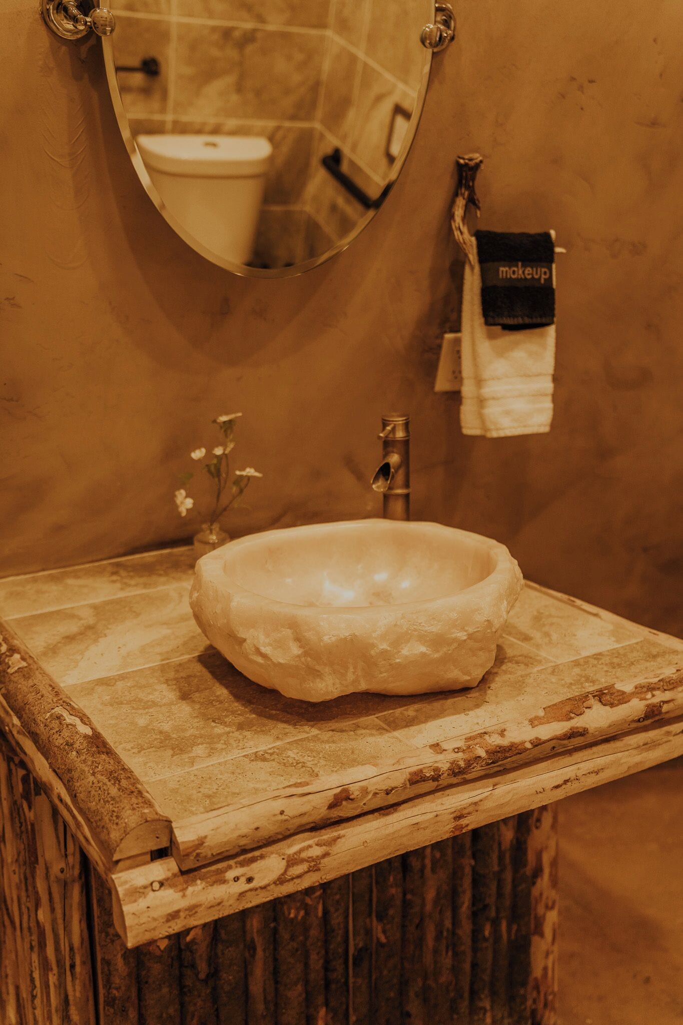 A bathroom with a rustic wooden vanity, a white ceramic sink, a mirror, and a towel rack with a 'makeup' towel.