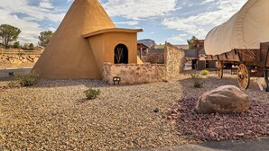 A traditional tipi with a stone base, a covered wagon, and a rocky terrain. - Zion White Bison (Virgin)
