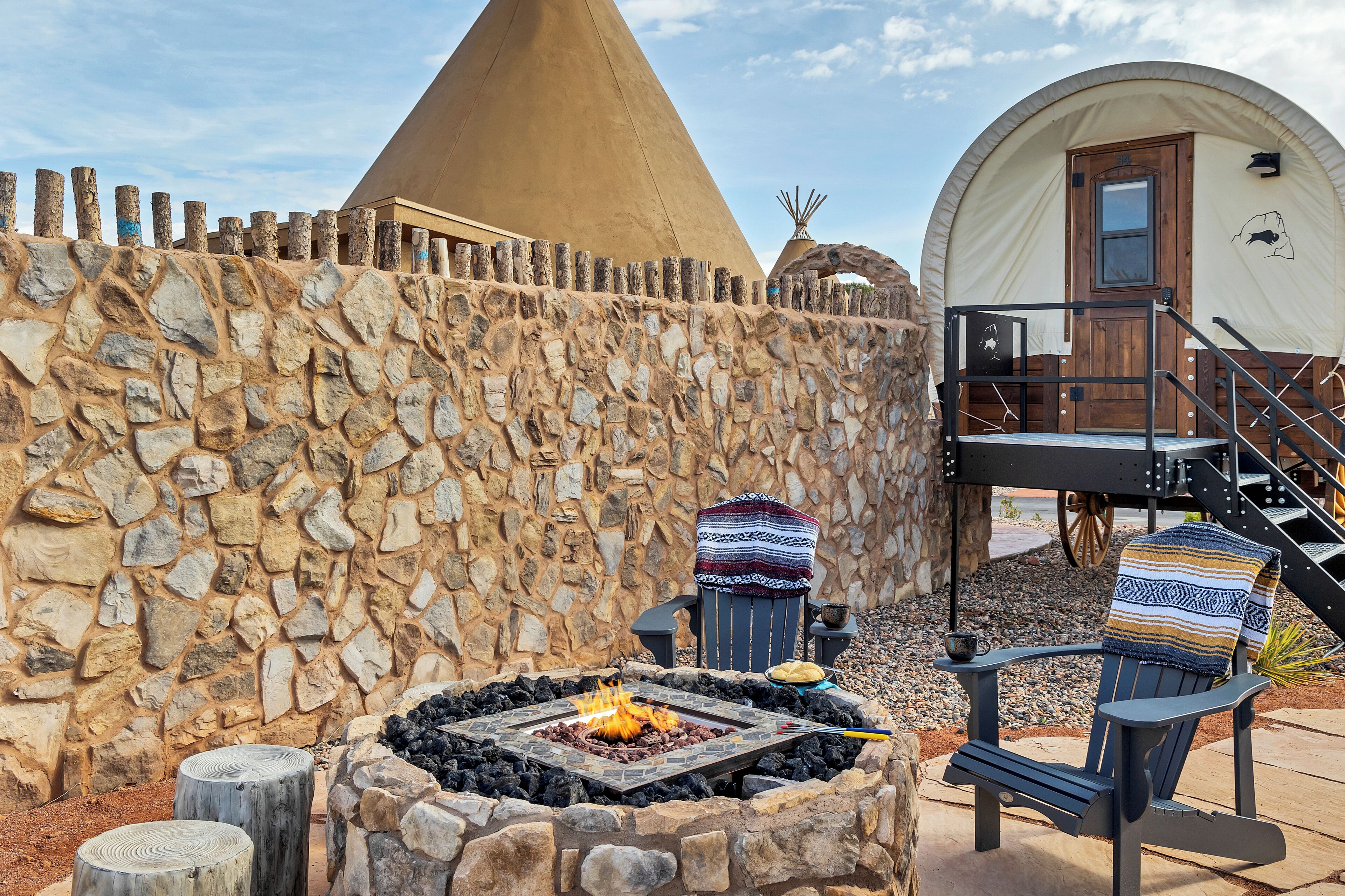 A stone wall, a fire pit, a teepee, and a covered tent.