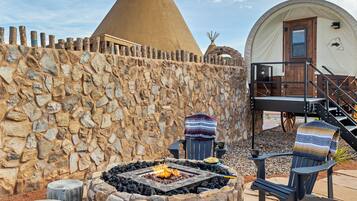 A stone wall, a fire pit, a teepee, and a covered tent.