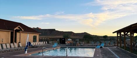 A pool area with lounge chairs and a hot tub, surrounded by buildings and a mountainous backdrop.