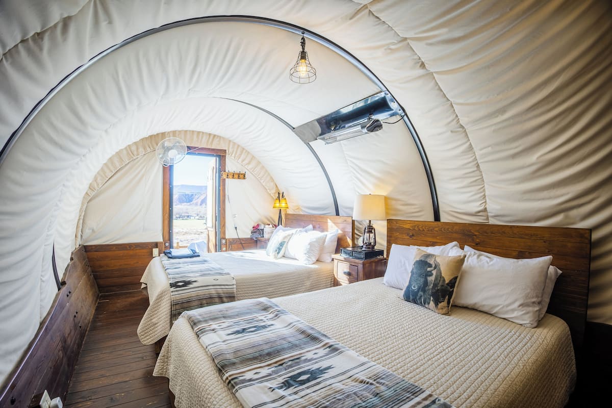 A cozy, circular tent-style room with two beds, wooden flooring, and a window providing a view of the outdoors.