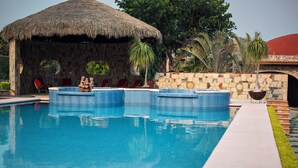 A swimming pool with a thatched-roof structure, stone walls, and red lounge chairs. - Ideal fifth for rest! Swimming pool, foosball, barbecue and much more. (San Gabriel las Palmas)