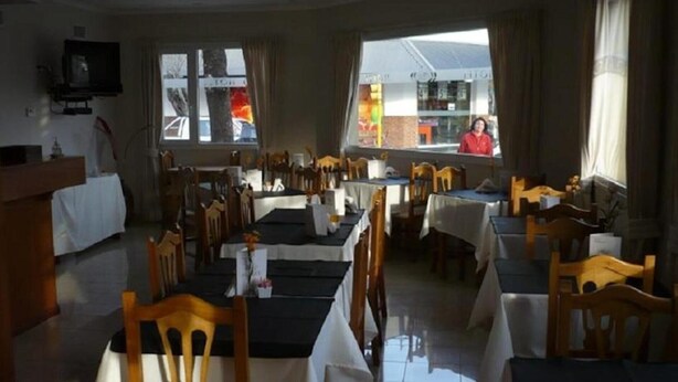 A restaurant with multiple tables and chairs, a TV mounted on the wall, and large windows with a view of the street. - Hotel Mirasierras (Tandil)