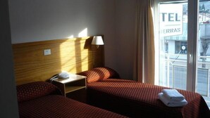 Una habitación de hotel con dos camas individuales, una mesita de noche con lámpara y una ventana con vista a la calle.