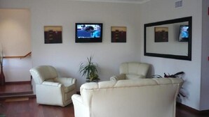 Un salón con dos sofás de cuero blanco, una planta en maceta y tres cuadros en la pared.