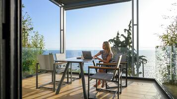 Una mujer trabajando en un ordenador portátil sobre una mesa en un balcón con vistas al mar.