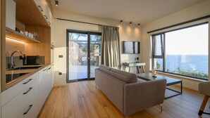 A modern kitchen with wooden cabinets, a built-in oven, and a dining area with a sofa and table. - VRAHOS Executive Suite, Mani Suites (Agios Dimitrios)