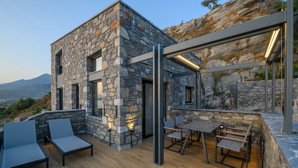Un bâtiment moderne en pierre, doté d’une terrasse en bois, d’un espace salon extérieur et offrant une vue sur le paysage.