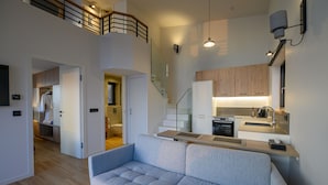 Un appartement moderne doté d’un espace de vie comprenant un canapé gris, une cuisine avec des meubles en bois et un escalier reliant les deux étages.