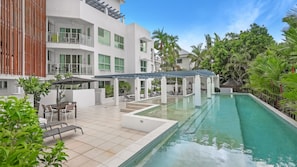 A pool area with a covered seating area, outdoor furniture, and a building with multiple balconies.