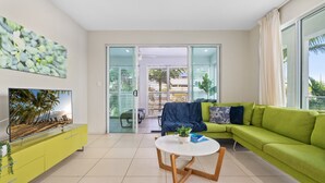 Un salon moderne avec un canapé vert, une table basse et un téléviseur posé sur un meuble jaune.
