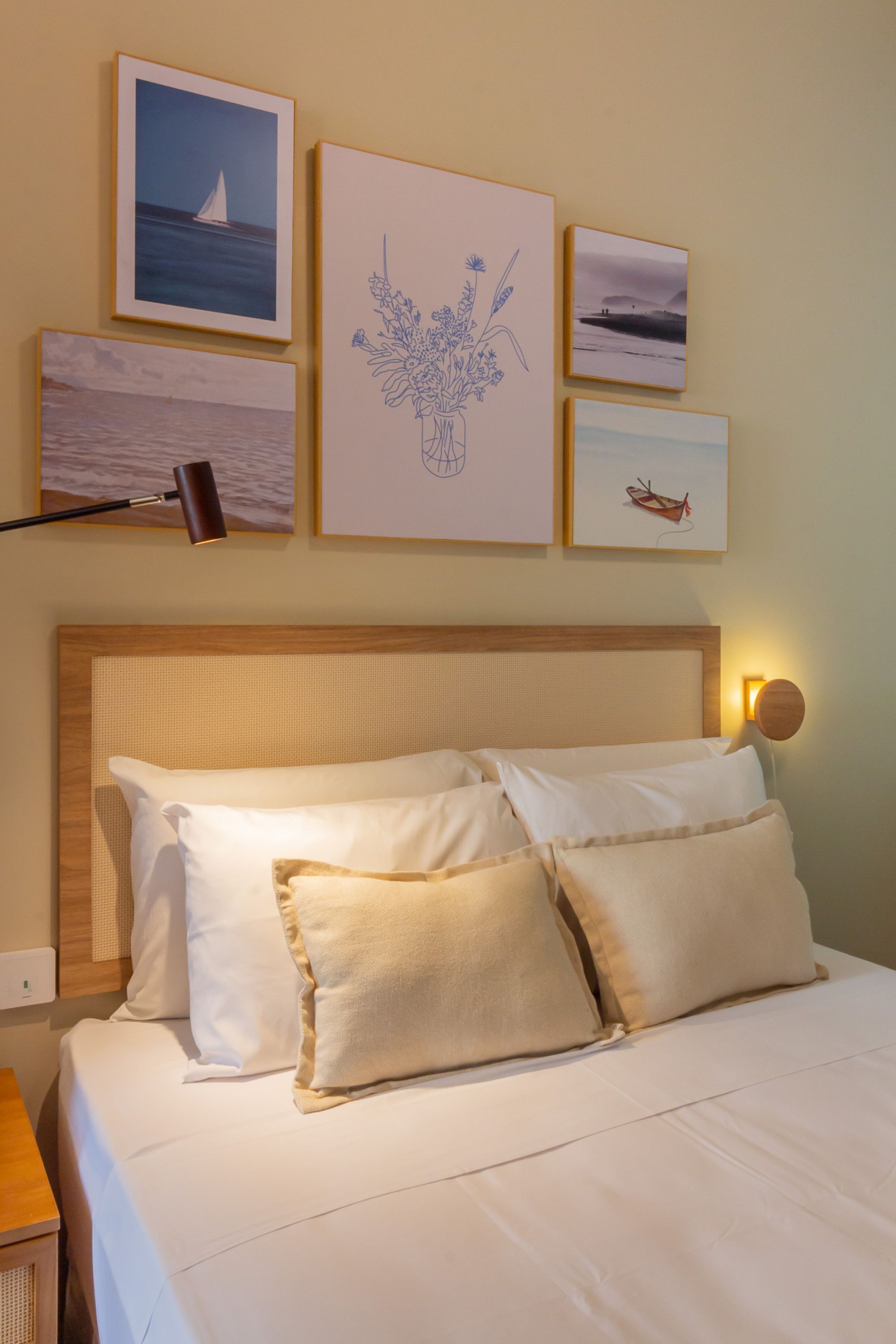 Una cama bien hecha con ropa de cama blanca y beige, un cabecero de madera y una lámpara fijada a la pared.
