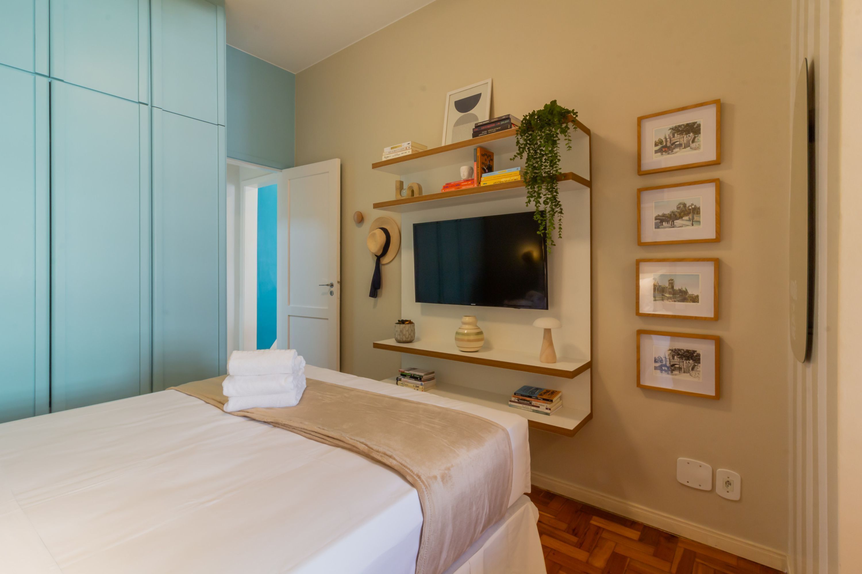 A bedroom with a bed, a television, shelves with books and decorative items, and a door leading to another room.