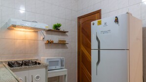 Una cocina con paredes de azulejos blancos, un refrigerador blanco, un microondas, una estufa a gas y una puerta de madera.