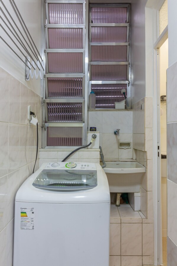 A compact laundry area with a washing machine, a sink, and a window with metal blinds.