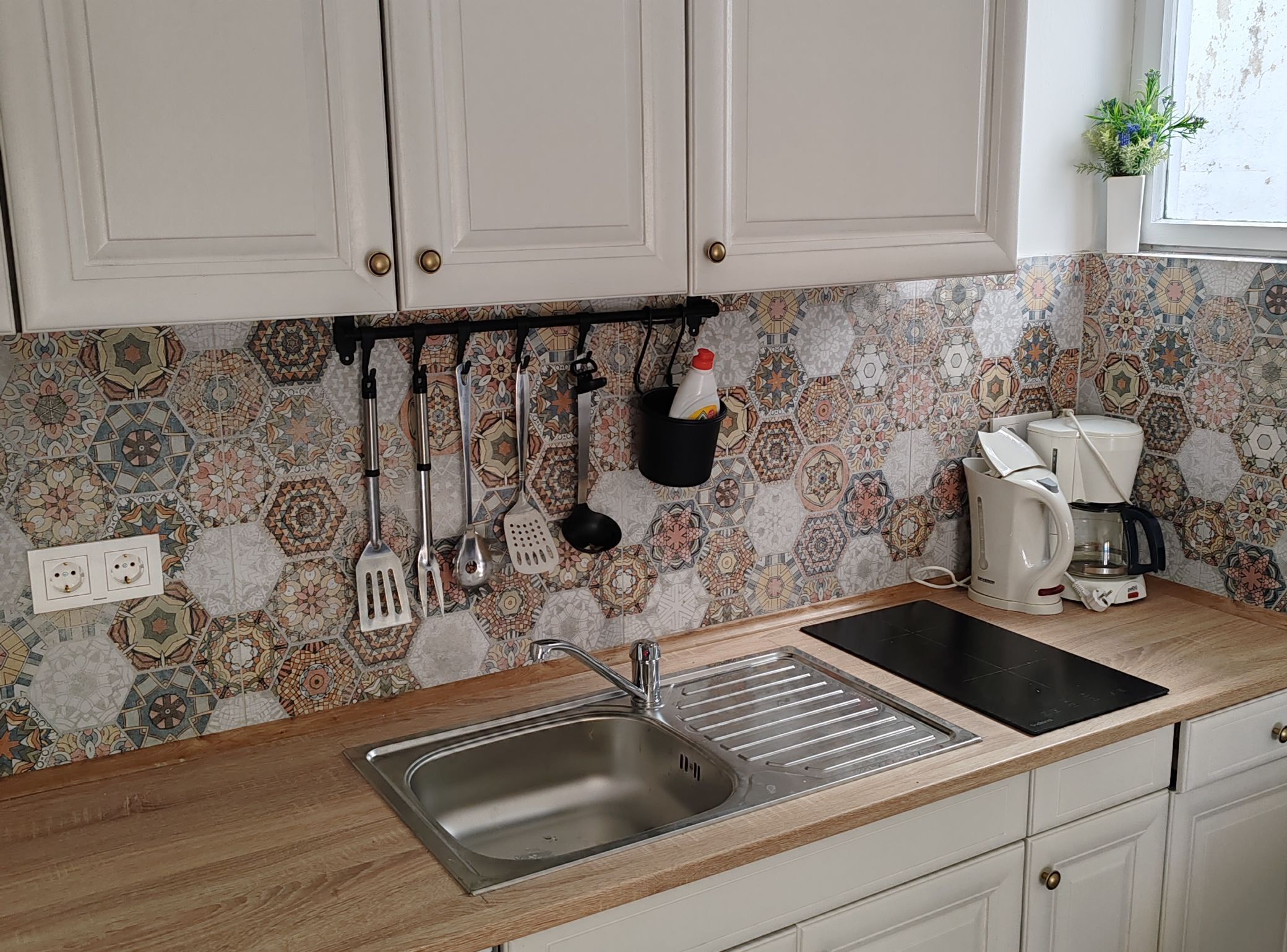 A kitchen with white cabinets, a stainless steel sink, a coffee maker, and various utensils hanging on a rack.