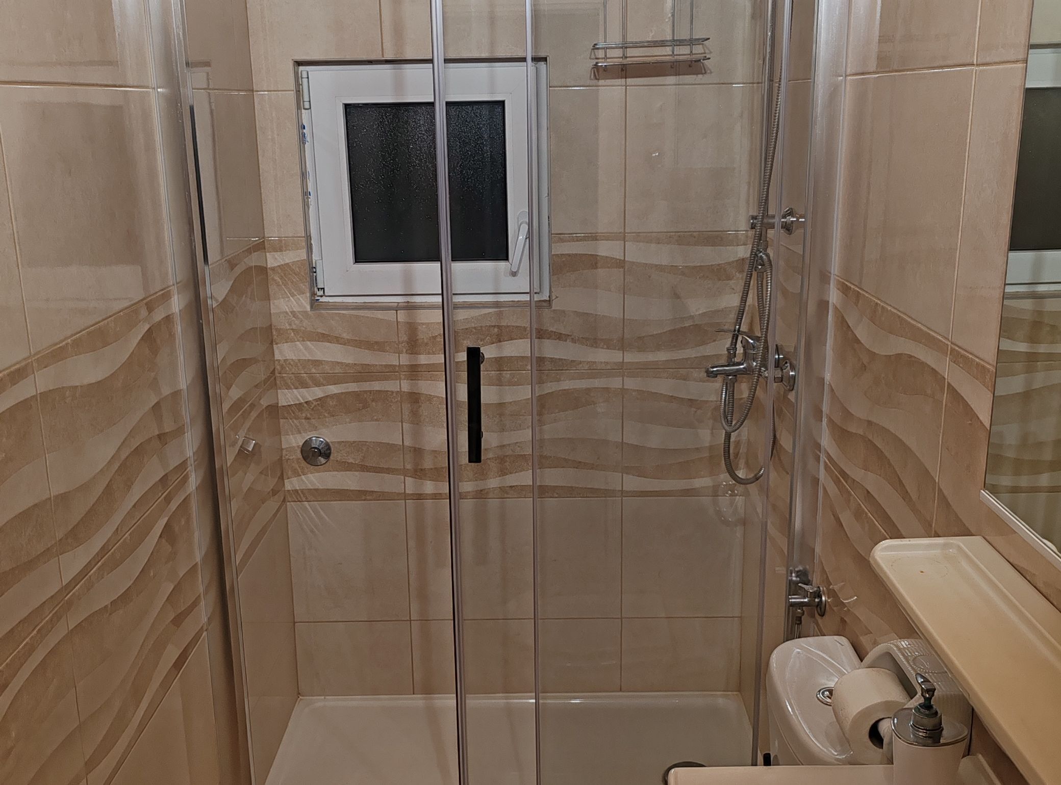 A shower enclosure with a glass door, a small window, and a handheld showerhead.